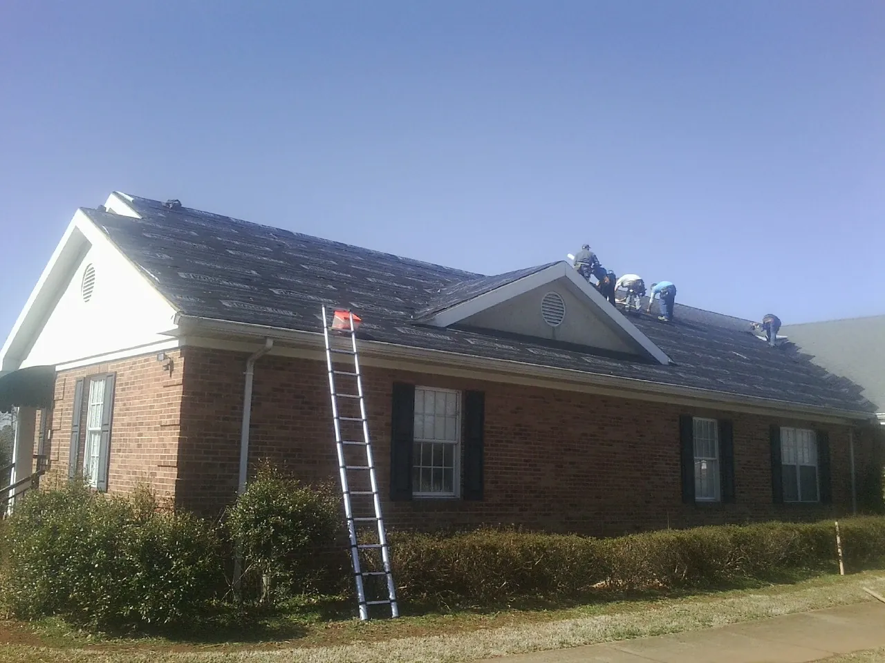 Crew tearing shingles off a brick ranch roof with a ladder set — Metal Roof Repair work by our crew in Vidalia