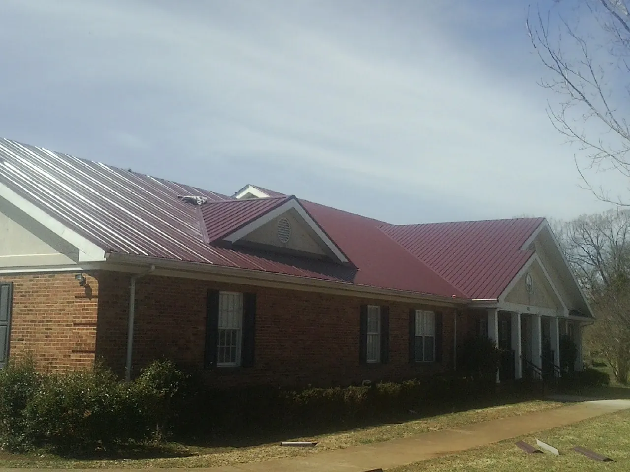 Red metal roof with gabled entries on a long brick building, from a Hail Damage Roof Repair job in Vidalia