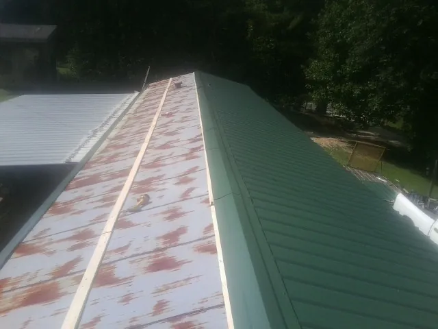 Old rusted panels beside newly installed green metal roofing — Wind Damage Roof Repair by Roofing Brothers in Vidalia