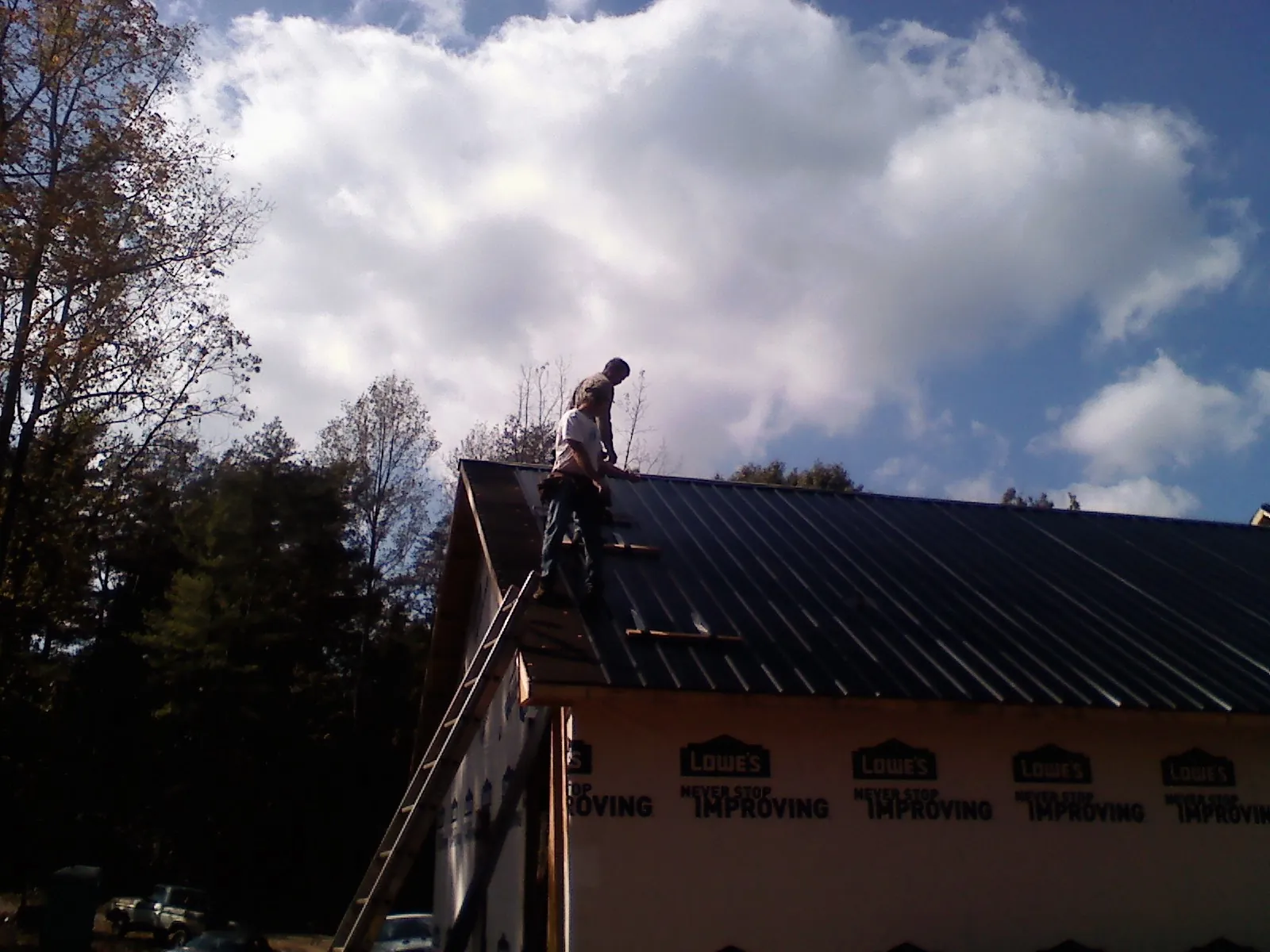 Roofer fastening dark metal panels high against a cloudy sky, from a Roof Inspection job in Vidalia