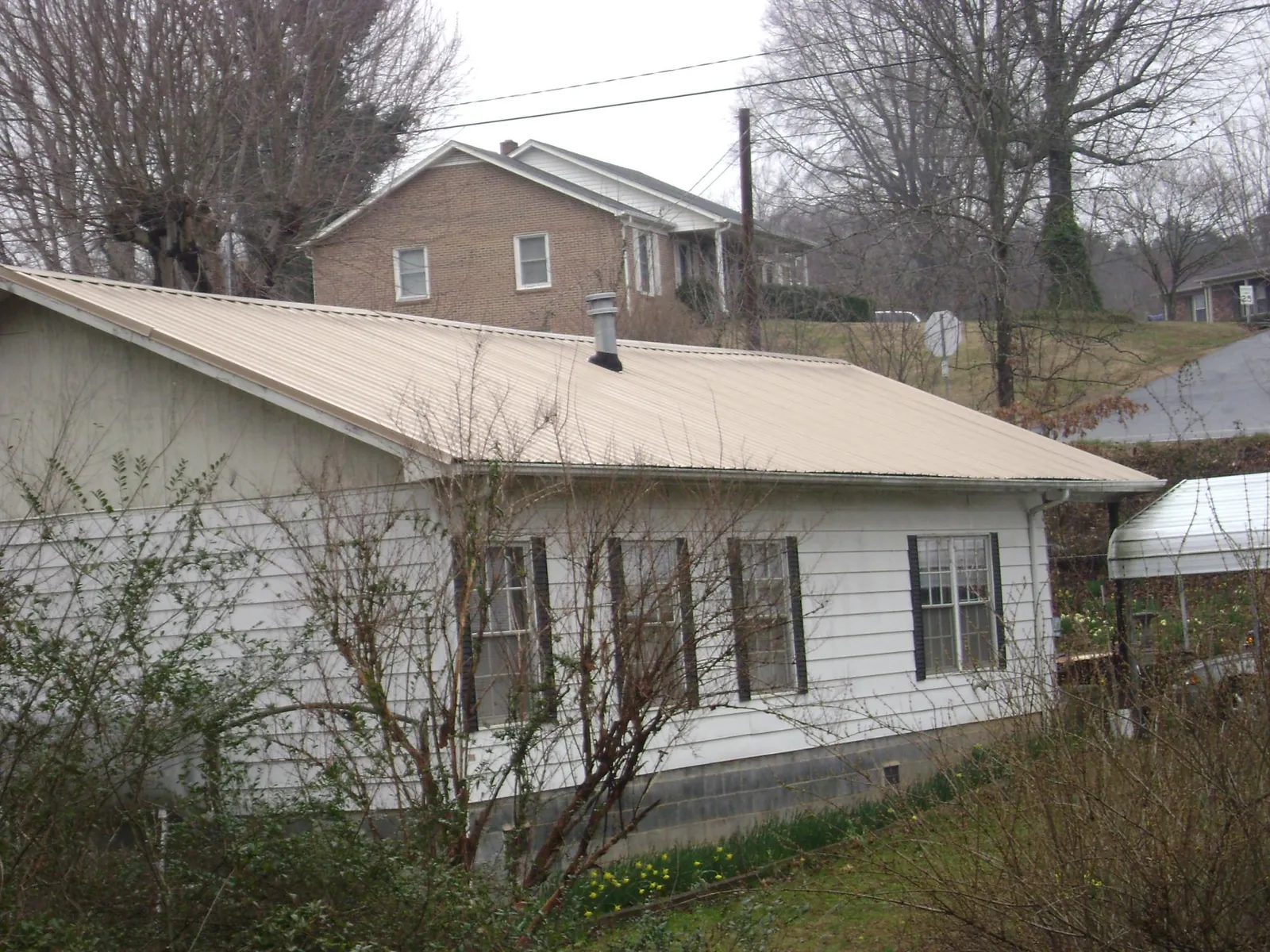 Tan metal roof on a white sided house set into a hillside — Commercial Roofing by Roofing Brothers in Vidalia